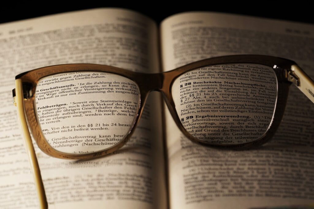 Ein Paar Brillen liegt auf einem aufgeschlagenen Buch, wobei der Text der Seiten durch die Gläser gut zu erkennen ist.