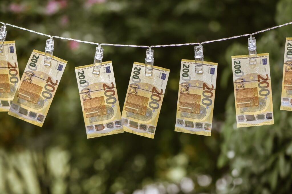 Ein Wäscheleine mit mehreren befestigten 200-Euro-Scheinen im Freien, vor einer unscharfen grünen Hintergrundlandschaft.